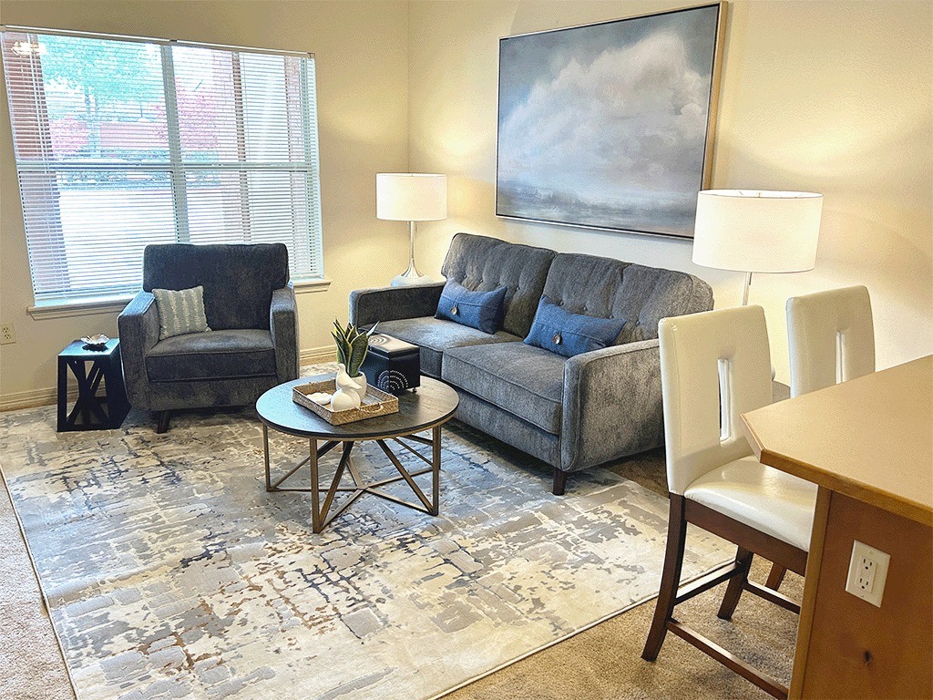 A living room with a grey couch, a black chair, a coffee table, and a painting on the wall.